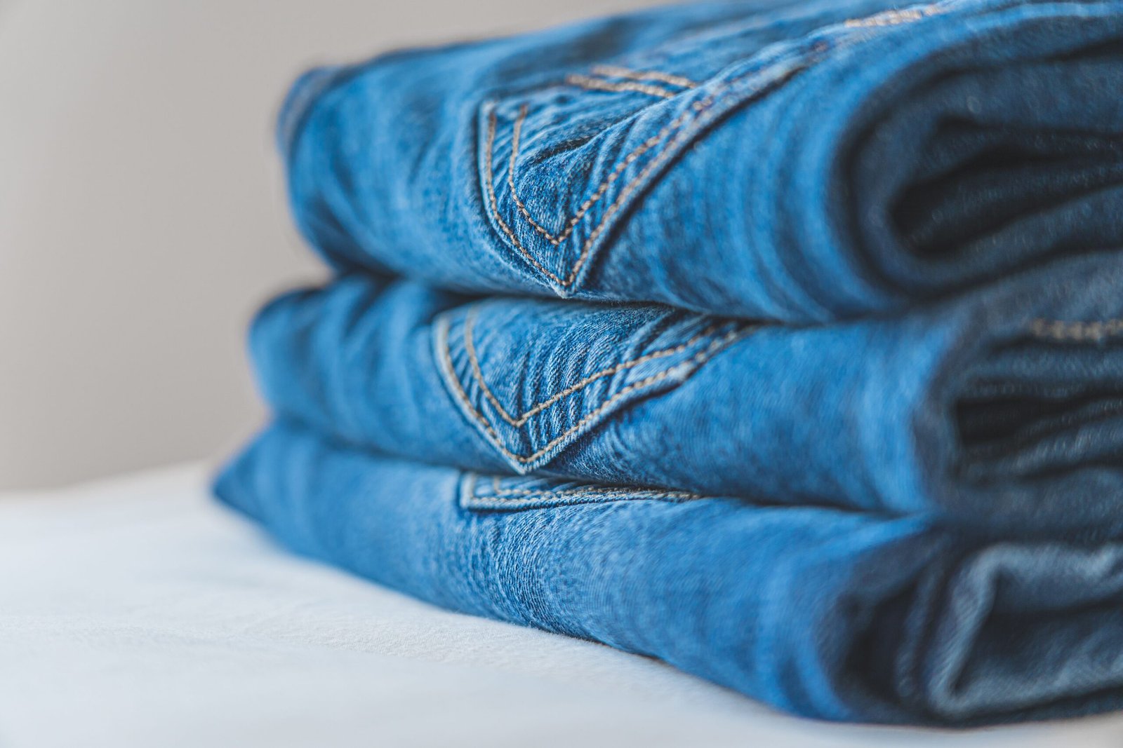 Stack of folded blue denim jeans on a white surface